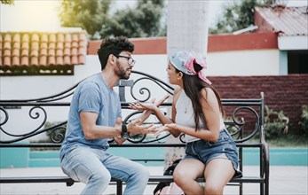 Man arguing with his girlfriend sitting in a park. Young couple arguing sitting on a park bench,