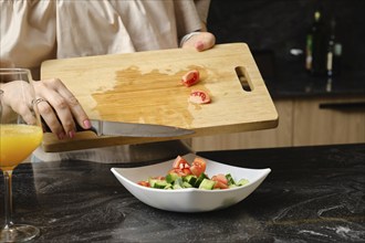 Closeup of hands of woman dropping a sliced tomato into a dish with salad