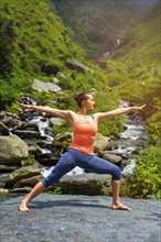 Yoga outdoors, sporty fit woman doing Ashtanga Vinyasa Yoga asana Virabhadrasana 2 Warrior pose