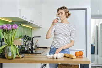 Beautiful young woman drinks water before making breakfast in her kitchen