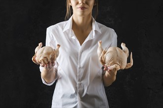 Unrecognizzable woman holds raw chicken in one hand and little chick in another