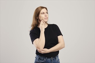 Young woman in black t shirt and jeans thinking over grey background