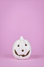 Pumpkin decoration with face on pink background with copy space