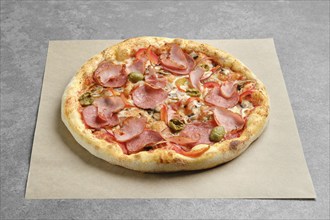 Pizza with ham, sausage, olives and bell pepper on parchment paper