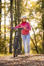 Woman pushing ebike through autumn forest, Black Forest, Gechingen, Germany, Europe