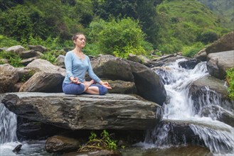 Woman doing yoga meditation asana Padmasana lotus pose outdoors at tropical waterfall