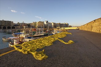 Morning light, yellow fishing nets, fishing boats, houses, blue sky, few white clouds, harbour,