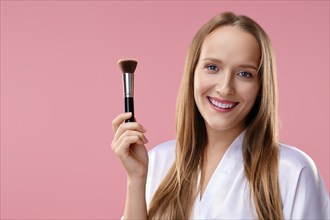 Beautiful girl with makeup brush in hand over pink background