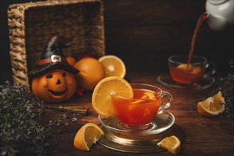 Tea with orange in cup, on wooden background, in front of Halloween decoration