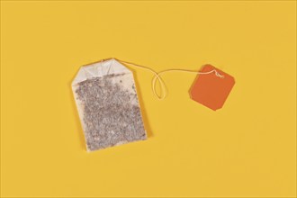 Tea bag with blank orange label on yellow background