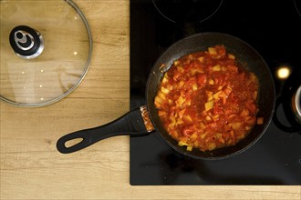 Overhead view of frying pan with tomato sauce on modern electric stove, the glass lid lies next to