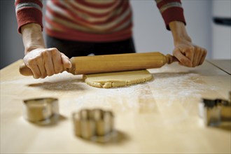 Unrecognizable woman rolls out ginger dough with rolling pin on kitchen table (low angle view with