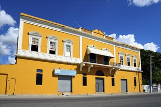 Two-storey yellow building under a clear blue sky with closed shop fronts, Church of Christ,