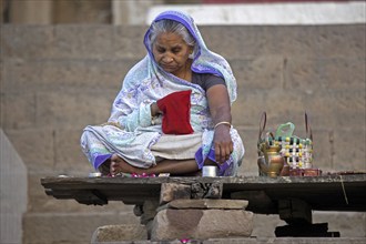 Old Indian woman sitting on ghat and praying near the Ganges river at Varanasi, Uttar Pradesh,