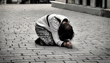 Social hardship, Torn beggar woman with poor clothes in humble posture kneeling on the street, KI