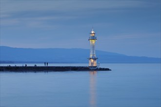 Tourists enjoying dusk next to the lighthouse by the harbour wall at the Lake Geneva basin, Canton