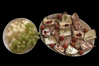 Plate with sandwiches and a plate with melon pieces and grapes on a black background,