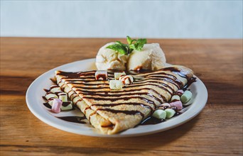 Close up of sweet crepe with ice cream on wooden table. Chocolate crepe with ice cream on wooden