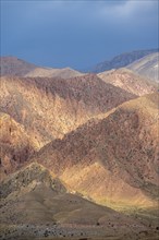 Red and orange mountains in atmospheric light, dramatic cloudy sky, mountain landscape near