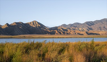 Blue Toktogul reservoir between dry mountain landscape, hilly mountains in the evening light,