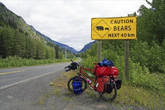 Bicycle standing in front of sign warning of crossing bears for the next 40 km, Stewart Cassiar