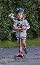 Boy with helmet, blond, 5 years, riding scooter, pink. Stuttgart, Baden-Württemberg, Germany,