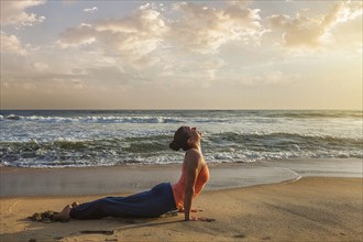 Yoga outdoors on beach, woman practices Ashtanga Vinyasa yoga Surya Namaskar Sun Salutation asana