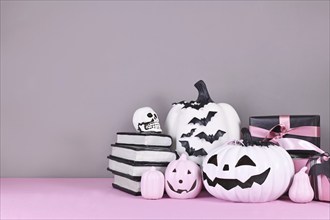 Pink and white Halloween decor with black and white pumpkins, spell books and spiders on gray