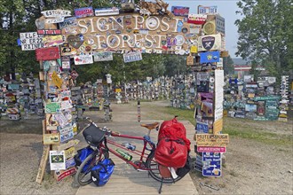 Bicycle with luggage in front of town and road signs in the signpost forest, cycling trip, cycling