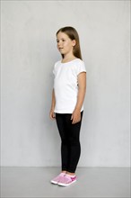 Cute young child with long hair in white t-shirt and black sweatpants posing