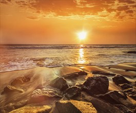 Tropical beach vacation background, waves and rocks on beach on sunset with beautiful cloudscape.