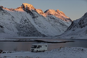 Motorhome in winter in front of snow-covered mountains illuminated by the sun, Lofoten, Norway,