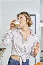 Young woman drinks cappuccino for breakfast at home, the plate with fried eggs and toasts stands on