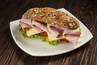 Ham sandwich with lettuce, cheese, tomato on plate on wooden table