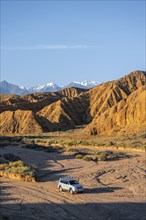 Off-road vehicle driving through a canyon, landscape of eroded hills at sunrise, badlands, white