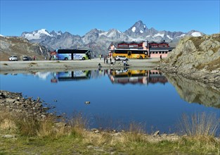 Coach with tourists and yellow bus of the Swiss PostBus AG on the Nufenen Pass, behind the mountain