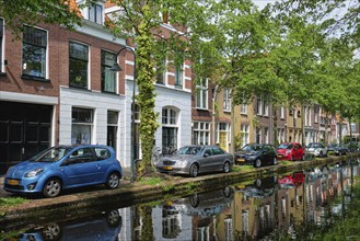 Delft, Netherlands, May 12, 2017: Cars and bicycles parked on canal embankment in street of Delft