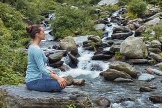 Woman in Hatha yoga asana Padmasana outdoors at tropical waterfall