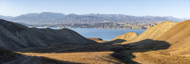 Panorama, blue Toktogul reservoir between dry mountain landscape, hilly mountains in the evening