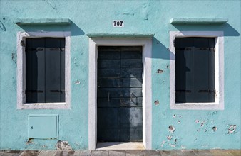 Light blue house facade with entrance door and windows with closed shutters, colourful houses on