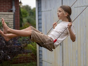 Boy swinging while sitting on children's swing at shed and garden gate, Germany, Europe