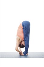 Woman doing Ashtanga Vinyasa Yoga asana Padangushthasana, standing forward bend hand to toe pose