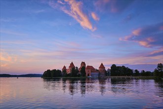 Trakai Island Castle in lake Galve, Lithuania on sunset with dramatic sky reflecting in water.