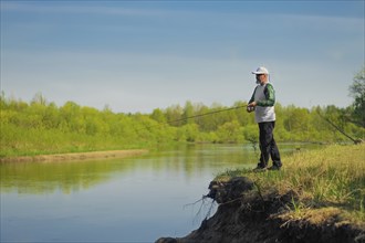 Man fish with spinning on river bank, casting lure. Outdoor weekend activity. Photo with shallow