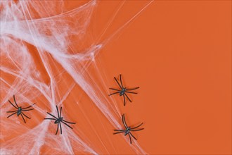 Cobweb and plastic spiders on side of orange Halloween background with empty copy space