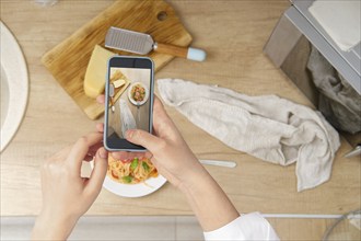 View from above of unrecognizable woman with smartphone taking photo of plate with pasta with