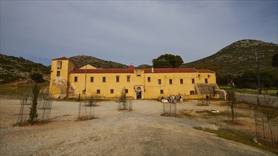 Fortress-like ochre building, façade, forecourt, enclosed trees, cloudy blue sky, Gouverneto,