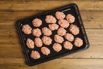 Top view of raw meatballs of minced meat on a baking tray on kitchen table