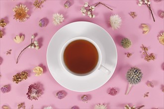 Cup of tea surrounded by flower decoration on pink background