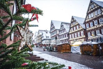 Christmas tree with decorations in front of a snow-covered half-timbered house at a market, Black